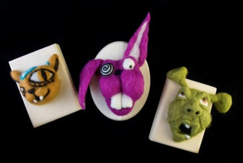3 felted wool creautres / animals on wooden plaques looking like fake taxidermy.. Left to right: an orange and teal cat with one  eyeball much larger than the other, Middle: a crazy magenta and white colored bunny, with one ear flopped over , big buck teeth and one googly eye in a spiral , Right: a green Shrek-like character with his mouth open